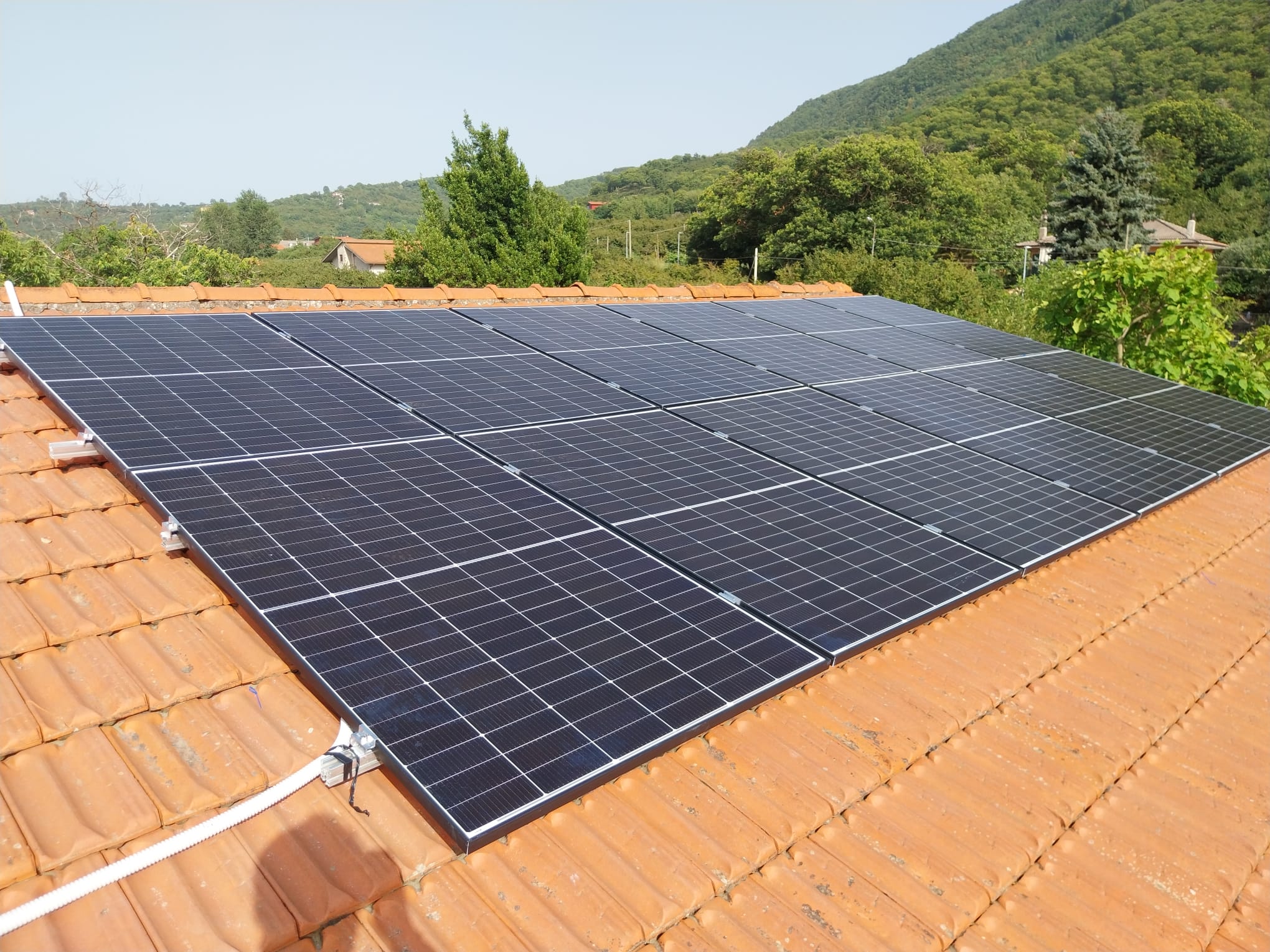 Vista frontale dell'impianto fotovoltaico su tetto con colline sullo sfondo